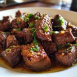 Close-up of tender crockpot steak cubes coated in a glossy brown sauce and garnished with parsley.