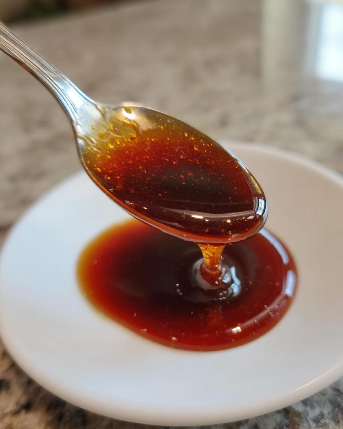 Close-up of thick, glossy homemade teriyaki sauce dripping from a silver spoon onto a white dish.