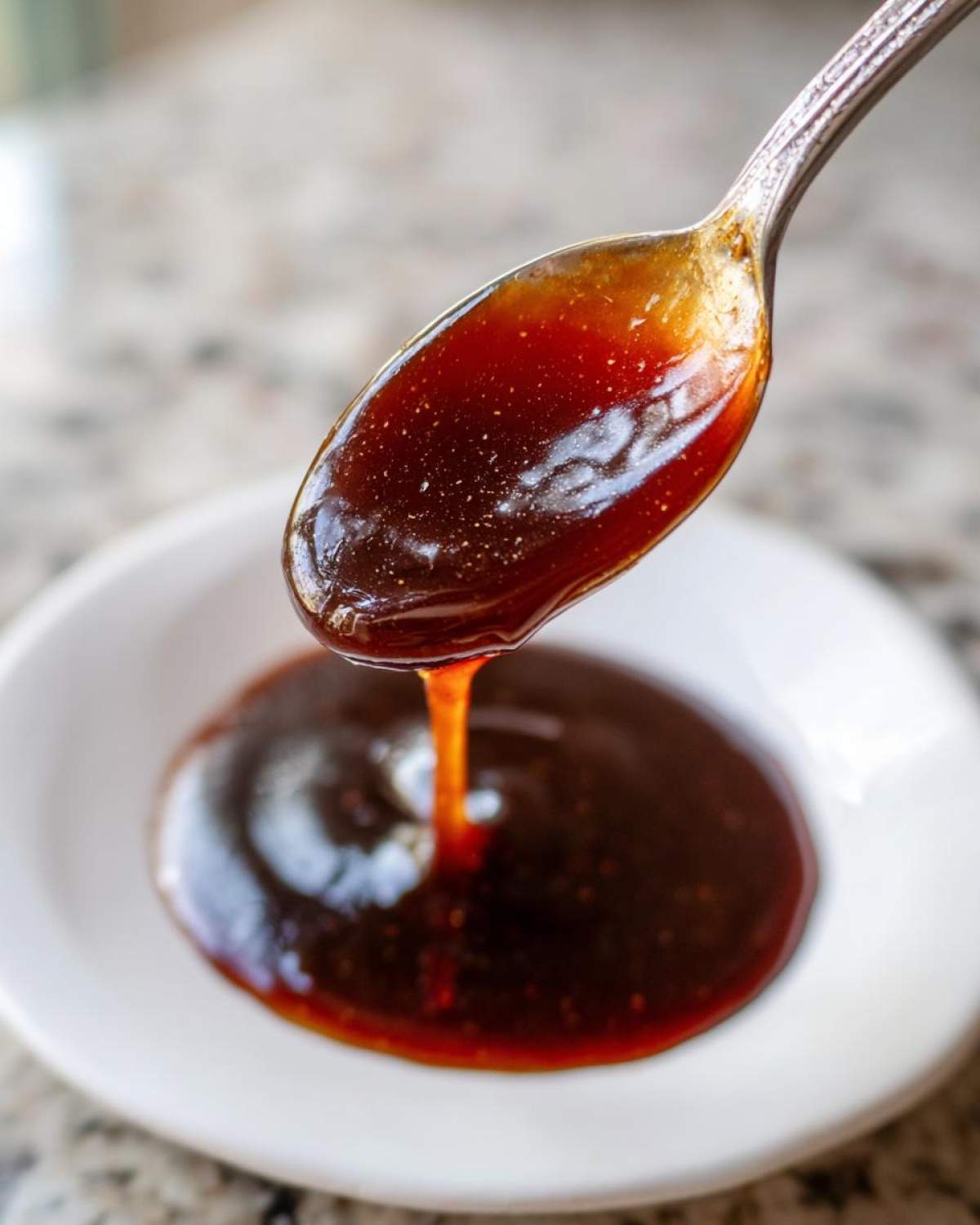 A spoonful of thick, glossy homemade teriyaki sauce dripping back into a white bowl.