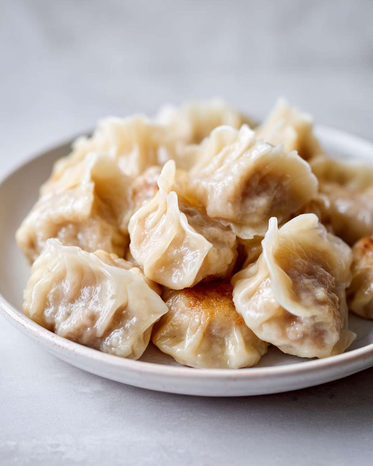 A close-up of a white plate filled with freshly cooked Traditional Chinese Dumplings, showing pleated wrappers and slightly browned bottoms.