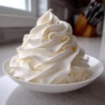 A tall, perfectly piped swirl of creamy white vanilla buttercream frosting in a small white bowl.