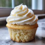 Close-up of a single, moist vanilla cupcakes topped with a swirl of creamy white frosting.