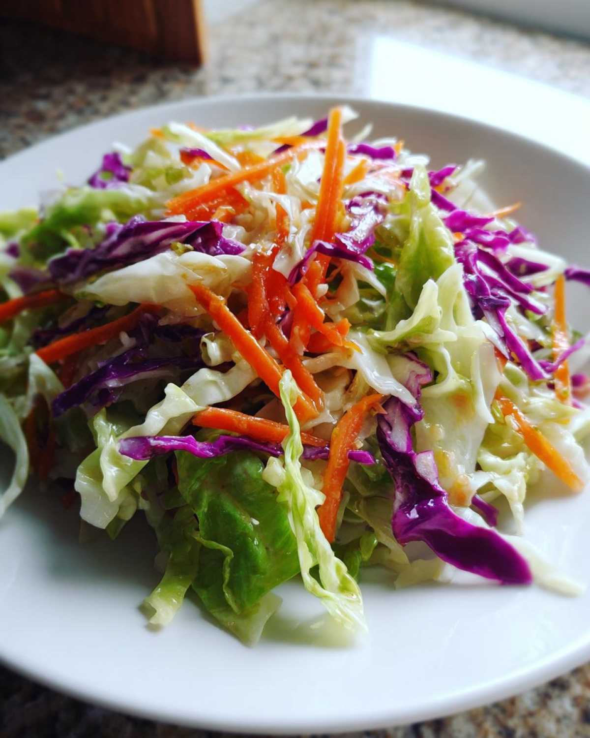 Close-up of a fresh cabbage salad featuring shredded green cabbage, red cabbage, and bright orange carrots.