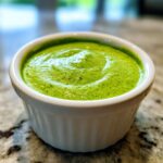 Close-up of bright green, creamy cilantro lime sauce served in a small white ramekin.