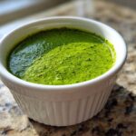 Close-up of bright green cilantro lime sauce blended smooth in a small white fluted ramekin.