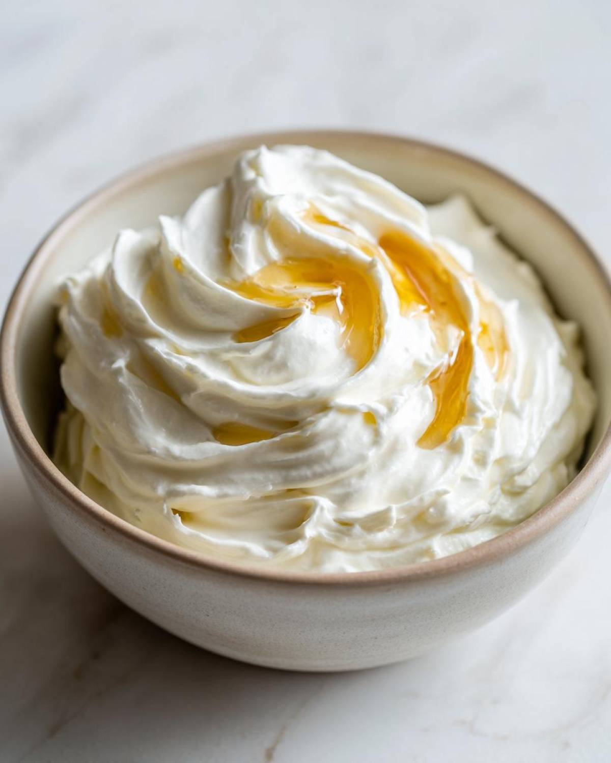 A close-up of creamy whipped feta dip topped with a drizzle of golden honey in a small bowl.
