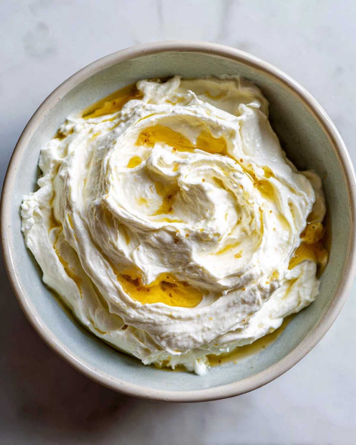 Overhead view of creamy whipped feta dip swirled in a light blue bowl, drizzled with golden honey.