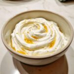 Close-up of creamy whipped feta dip swirled in a bowl, drizzled with honey and sprinkled with zest.