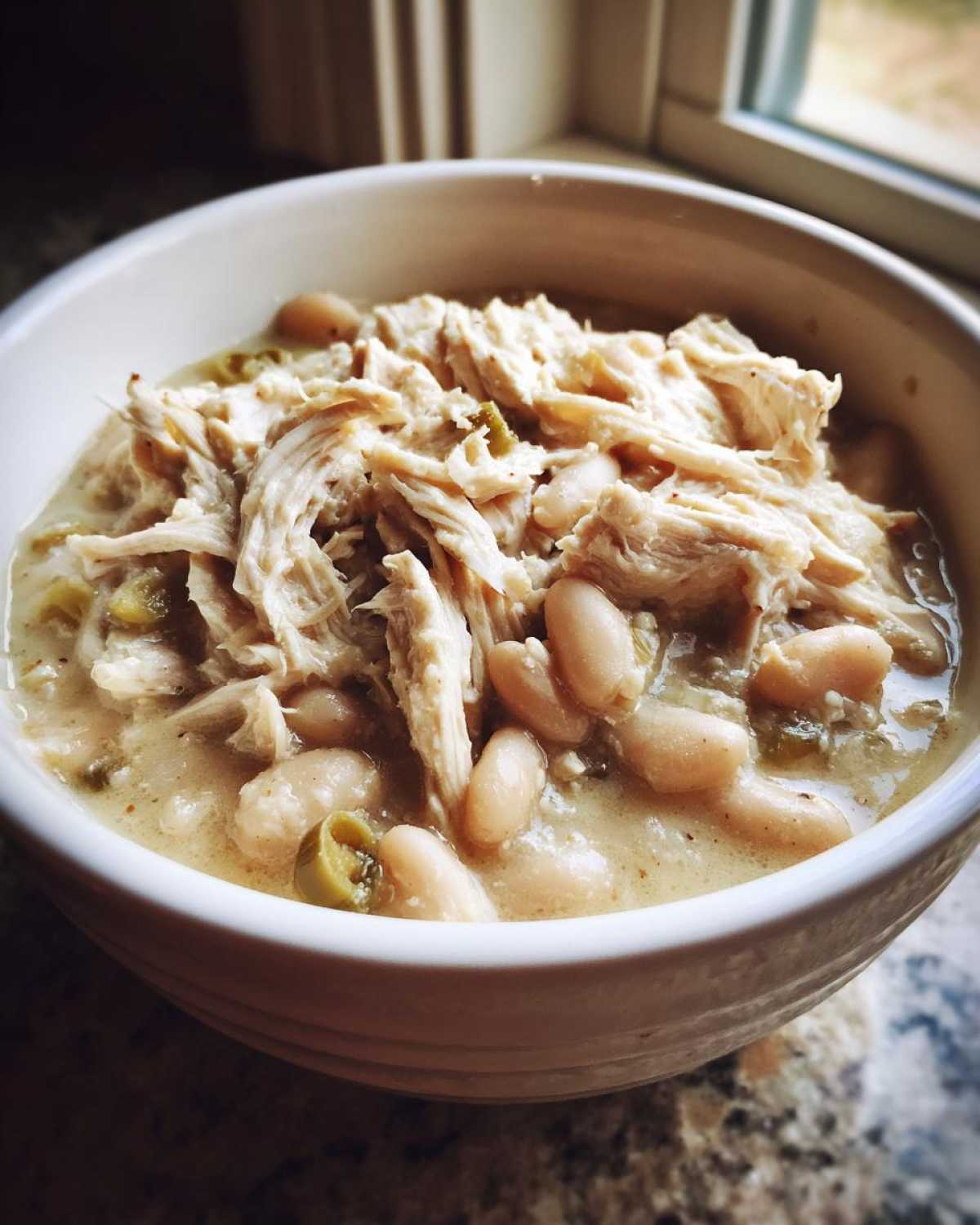 Close-up of a white bowl filled with creamy white bean chicken chili topped generously with shredded chicken.