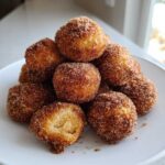A mound of golden brown Air Fryer Cinnamon Sugar Churro Bites heavily coated in sparkling cinnamon sugar on a white plate.