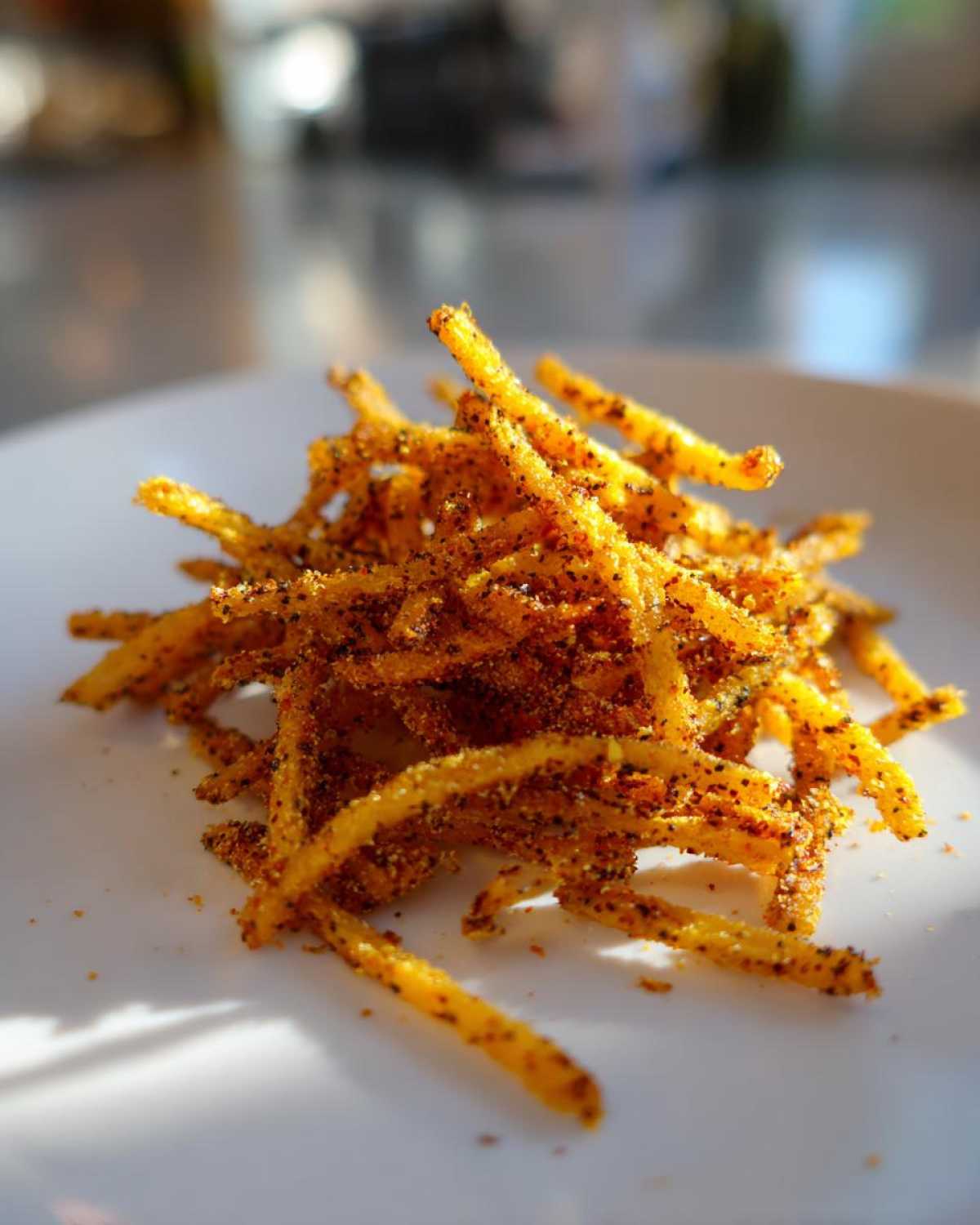 Close-up of seasoned, crispy Air Fryer Crispy Tortilla Strips piled on a white plate, catching the sunlight.
