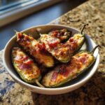 A white bowl filled with crispy Air Fryer Stuffed Jalapeno Poppers topped with melted cheese and bacon bits.