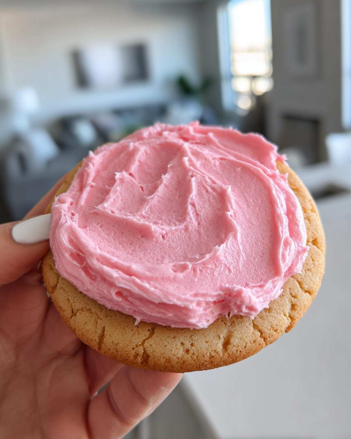 A hand holding a thick, chewy Copycat Crumbl Sugar Cookie topped with vibrant pink frosting.