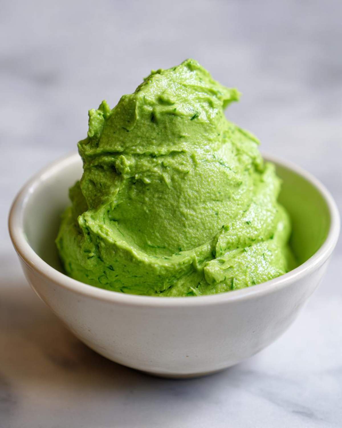A close-up of thick, vibrant green Copycat Panera Green Goddess Dressing mounded in a small white bowl.