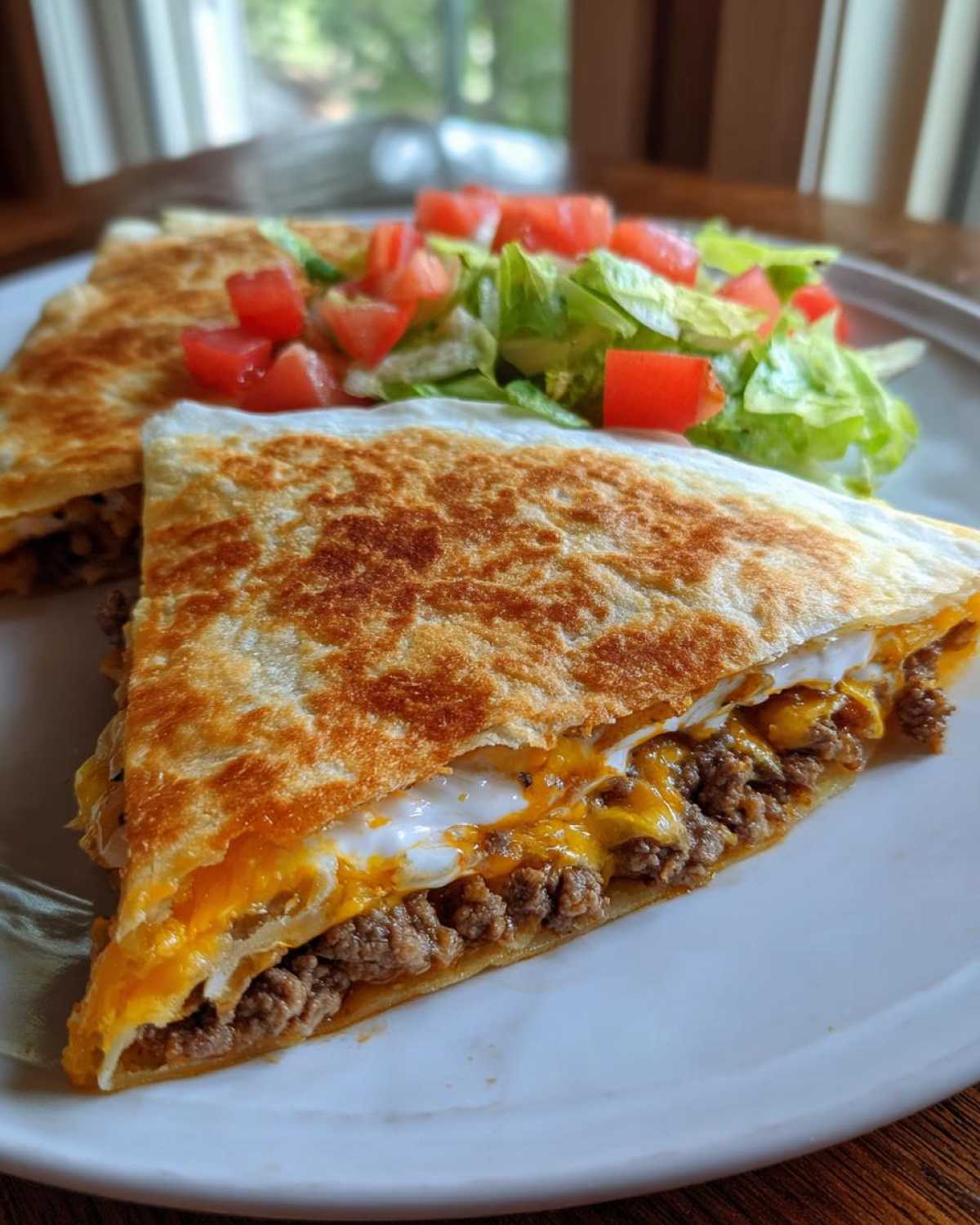A halved Copycat Taco Bell Crunchwrap Supreme showing seasoned ground beef, melted cheese, and sour cream, served with a side salad.