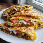 Four triangular slices of Copycat Taco Bell Crunchwrap Supreme stacked on a white plate, showing seasoned beef, cheese, lettuce, tomato, and sour cream.