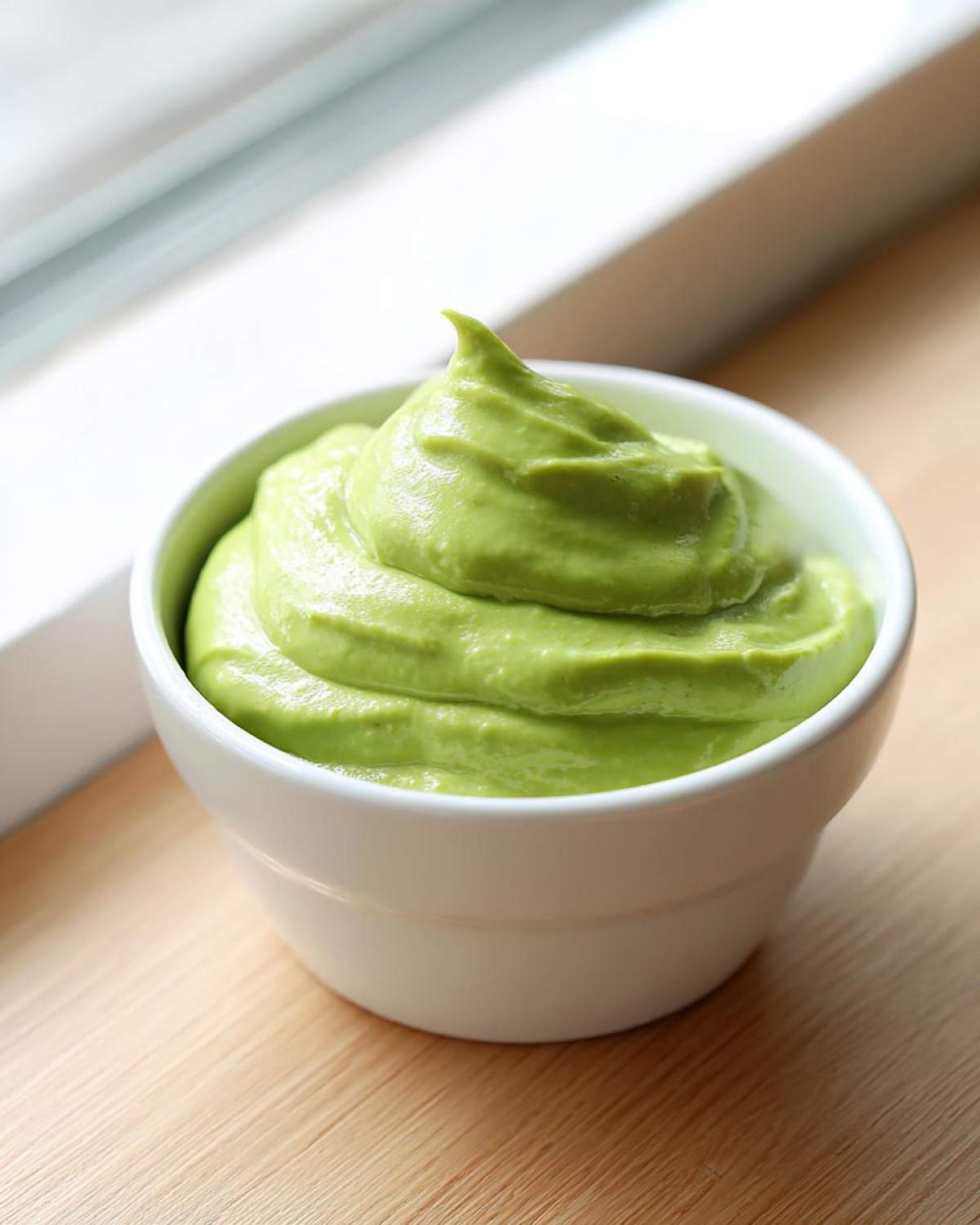 A small white bowl filled with bright green, smooth Creamy Avocado Cilantro Sauce, swirled high.