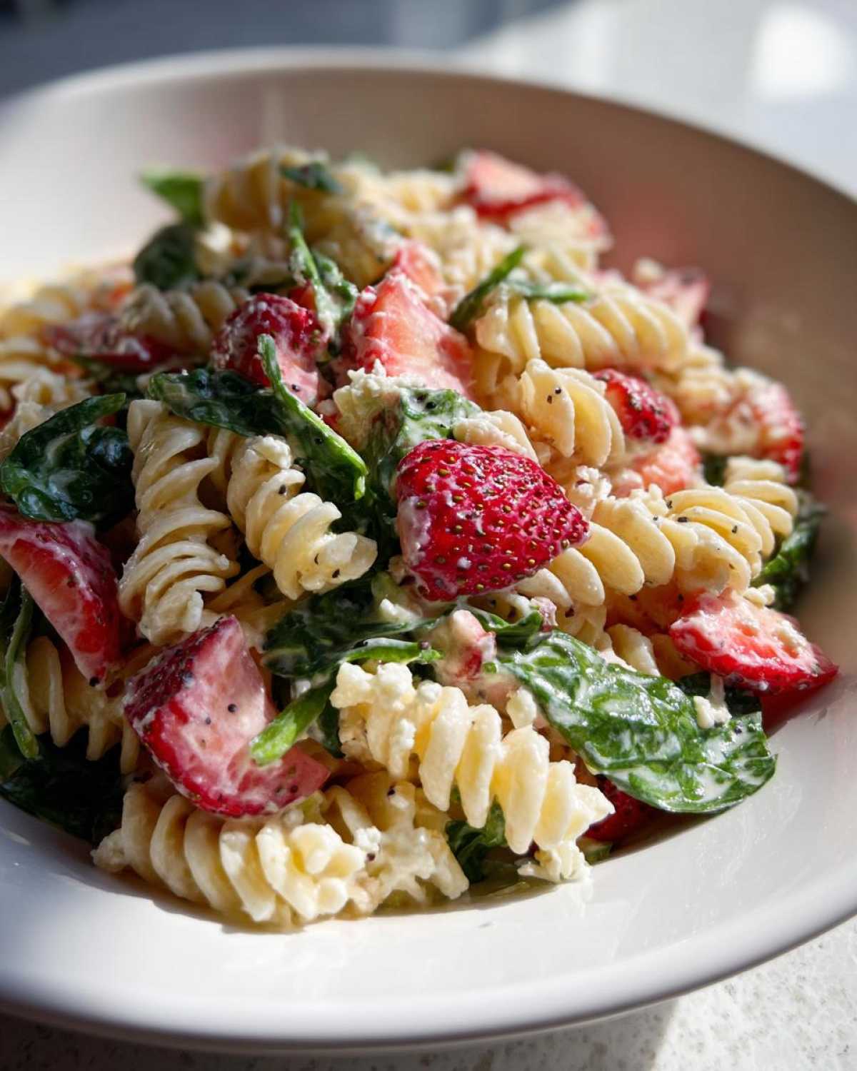 A close-up of Easy Strawberry Spinach Pasta Salad with Feta, featuring rotini pasta, bright red strawberries, and green spinach in a creamy dressing.