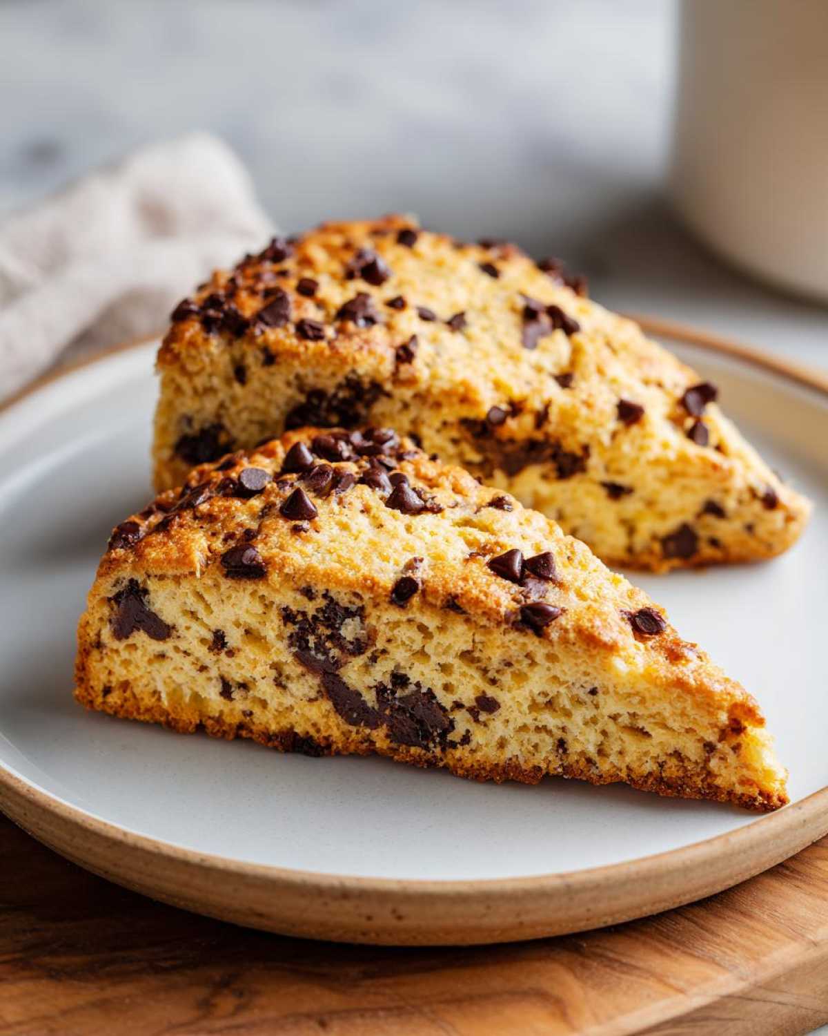 Close-up of two triangular Gluten-Free Chocolate Chip Scones on a light plate.