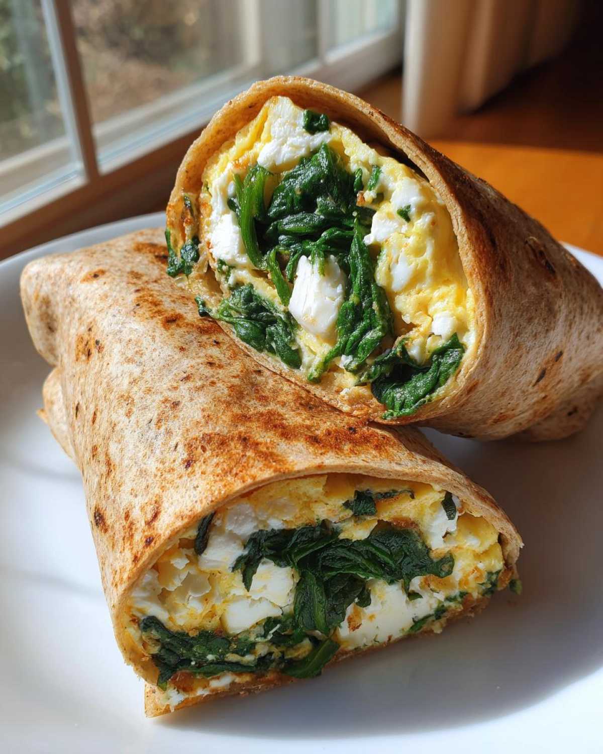 A whole wheat High-Protein Egg White Breakfast Wrap cut in half, showing egg whites, spinach, and cheese filling.