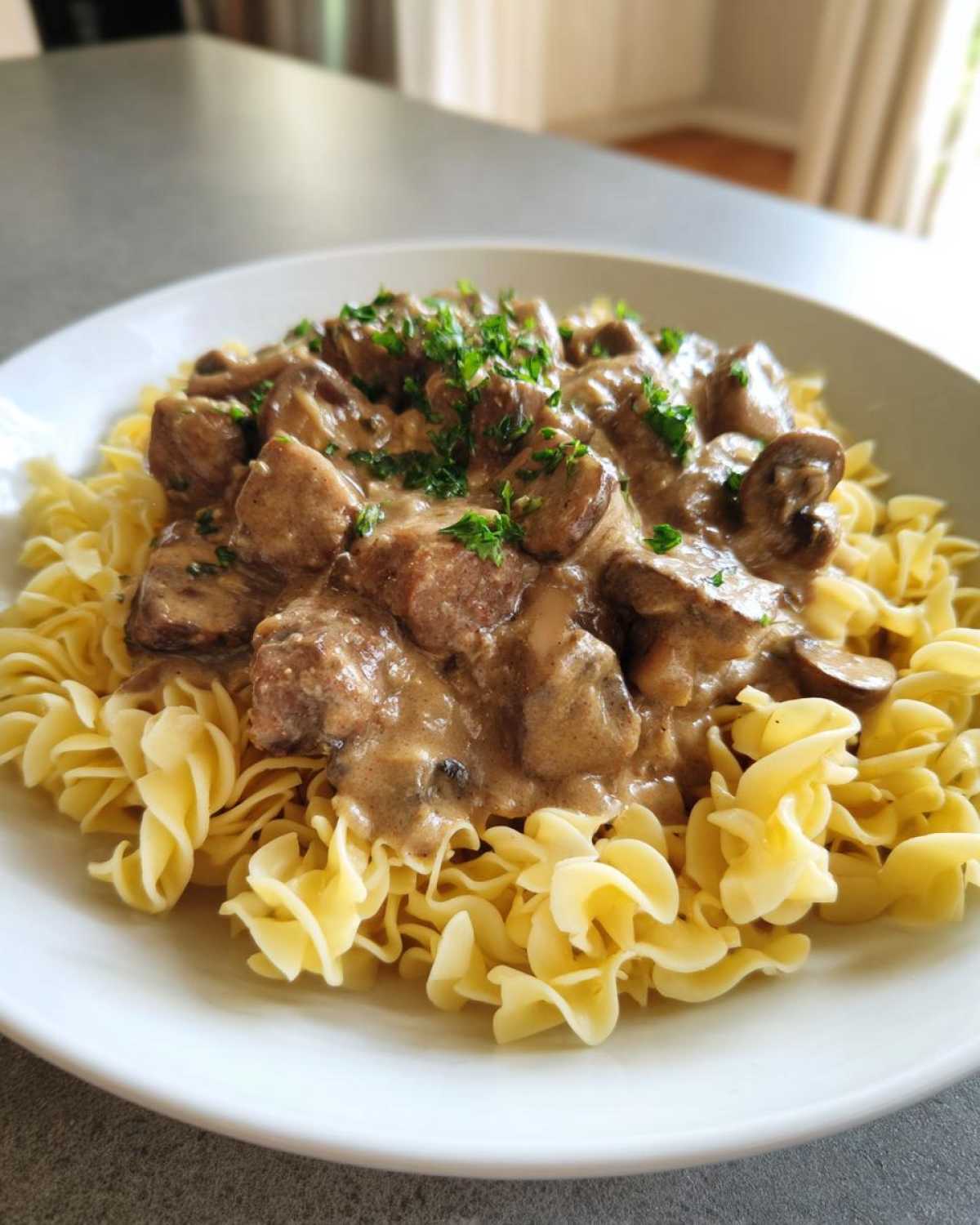 A serving of Instant Pot Beef Stroganoff with Mushrooms generously spooned over egg noodles and garnished with parsley.