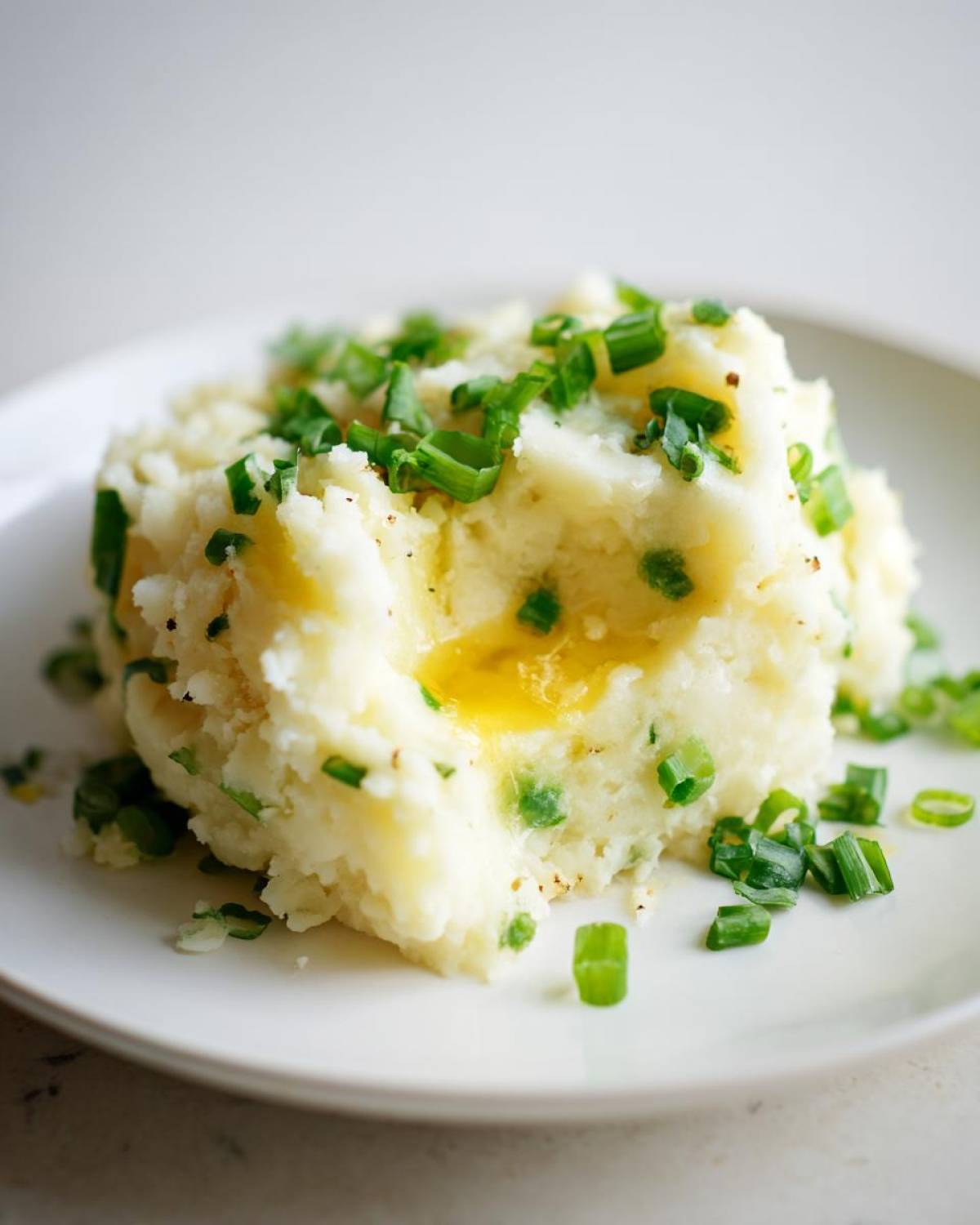 A serving of creamy Irish Champ mashed potatoes topped with fresh scallions and a pool of melted butter.