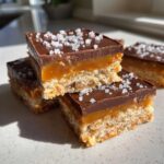 A stack of rich No-Bake Salted Caramel Pretzel Bars topped with dark chocolate and flaky sea salt.