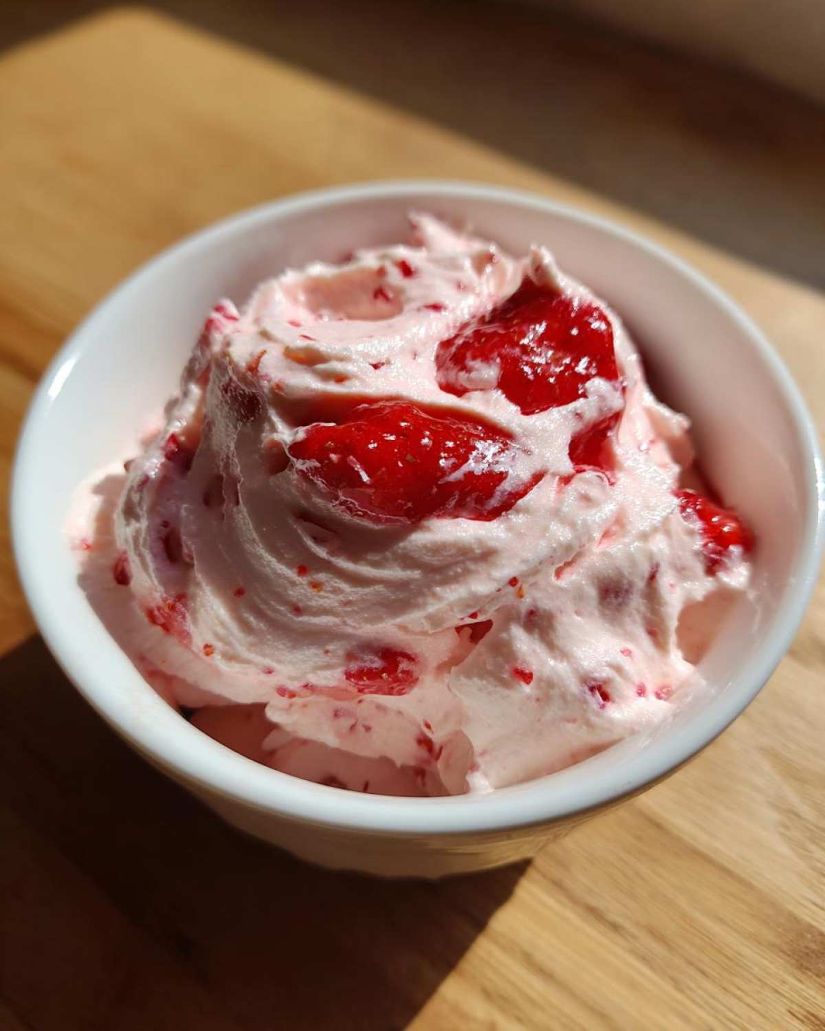 Close-up of creamy pink No-Bake Strawberry Cheesecake Dip topped with strawberry preserves in a white bowl.
