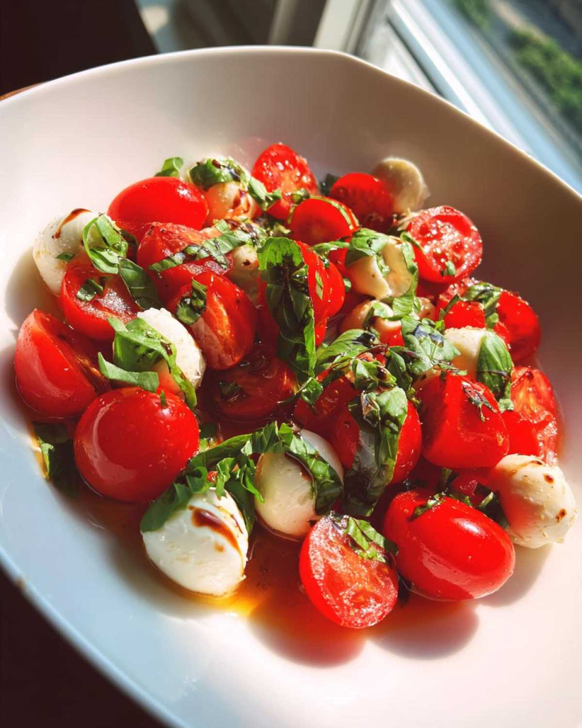 Close-up of a vibrant 15 Minute Caprese Salad featuring halved cherry tomatoes, small mozzarella balls, and fresh basil drizzled with balsamic glaze.