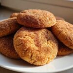 A close-up stack of freshly baked churro cookies coated generously in cinnamon sugar, resting on a white plate.