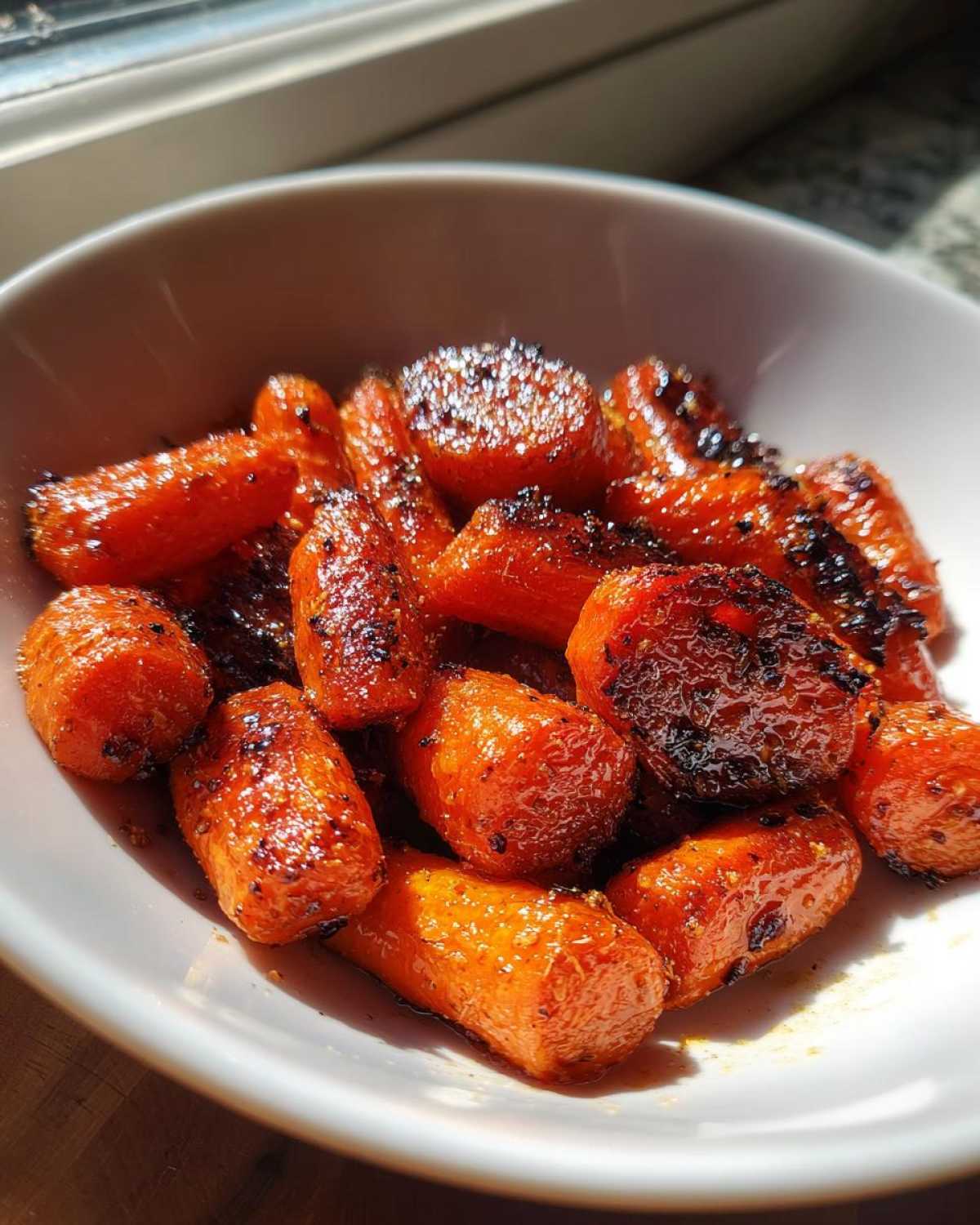 Close-up of sweet, glazed roasted carrots with caramelized edges served in a white bowl.