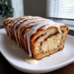 A freshly baked loaf of Amish Cinnamon Bread, sliced to show the swirl, covered in thick white icing.