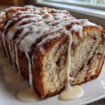A loaf of freshly baked Amish Cinnamon Bread with a thick, white vanilla glaze dripping down the sides.