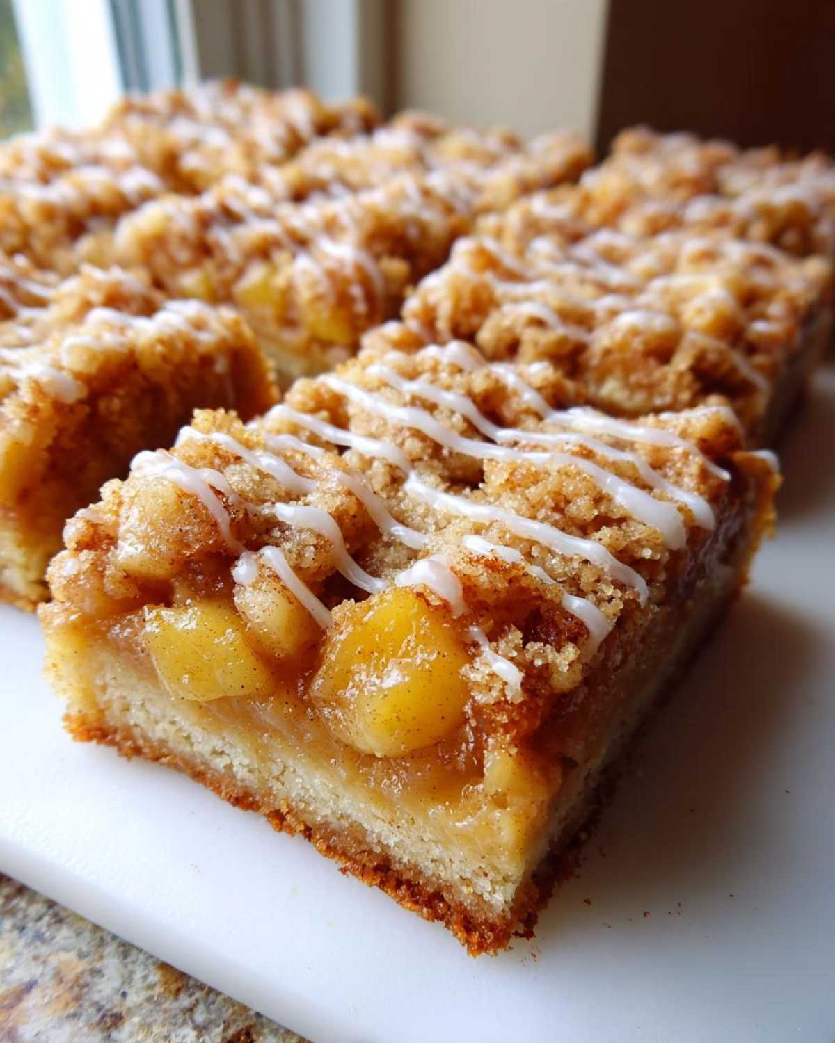 A close-up view of a freshly cut apple pie bars slice showing the thick apple filling, crumb topping, and white icing drizzle.