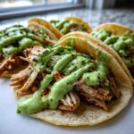Four soft tacos filled with shredded chicken and generously drizzled with bright green Avocado Lime Crema.