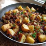 Close-up of perfectly browned Bacon and Onion Skillet Potatoes garnished with fresh parsley in a dark pan.