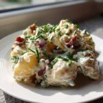 A close-up of creamy Bacon & Blue Cheese Potato Salad topped with crispy bacon bits and fresh chives.