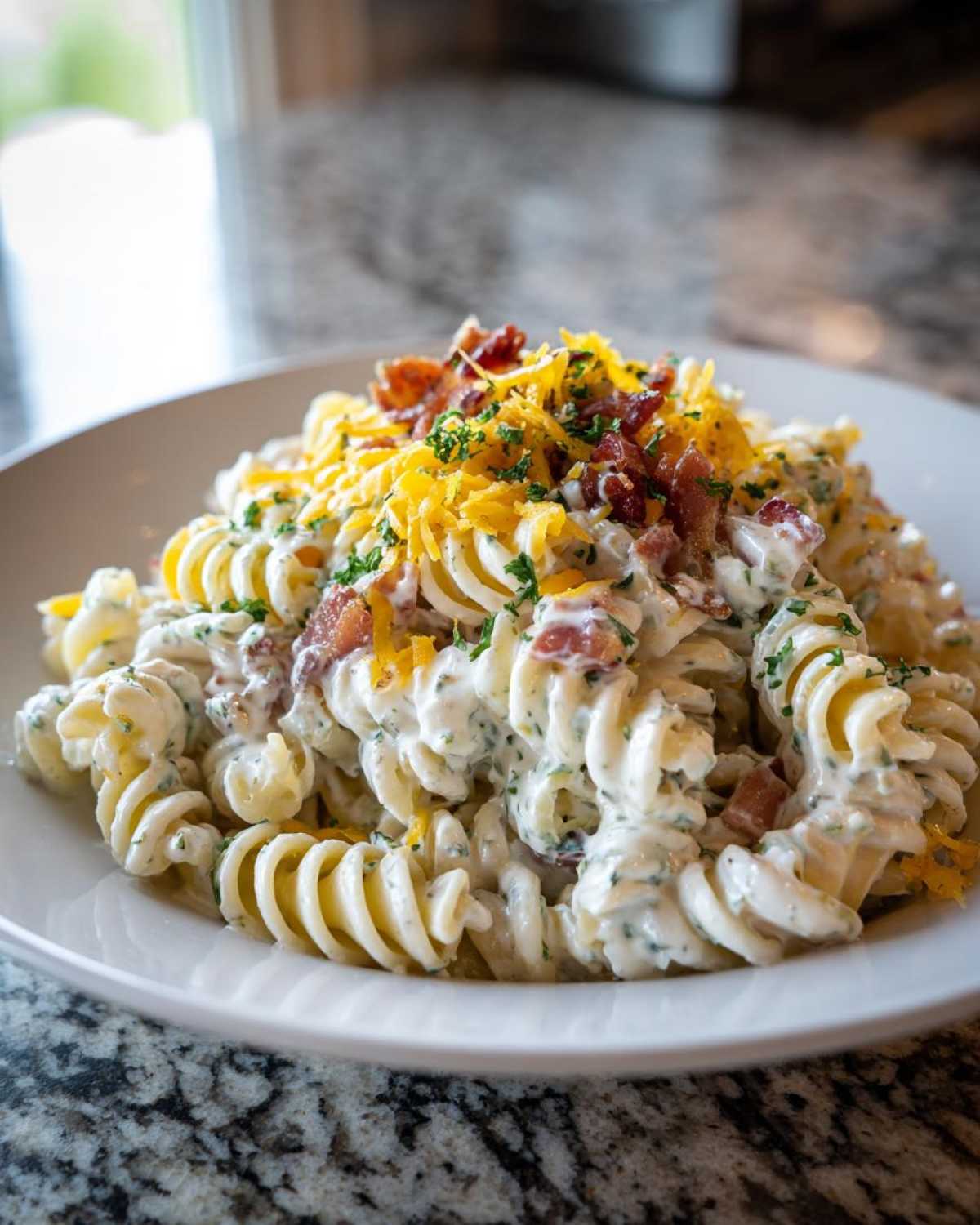 A close-up of creamy Bacon Ranch Pasta Salad made with rotini pasta, topped with bacon bits, shredded cheddar cheese, and parsley.