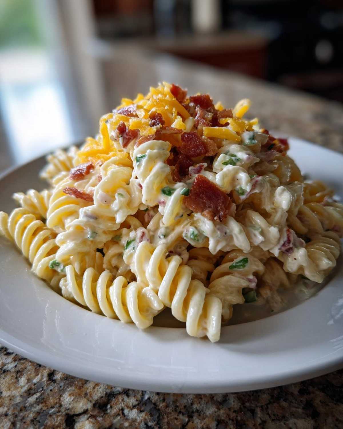 A close-up of a serving of Bacon Ranch Pasta Salad made with rotini pasta, creamy dressing, bacon bits, and topped with shredded cheddar cheese.