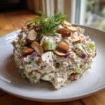 A mound of creamy Baked Marinated Chicken Salad mixed with red onion and celery, topped with sliced almonds and fresh dill.