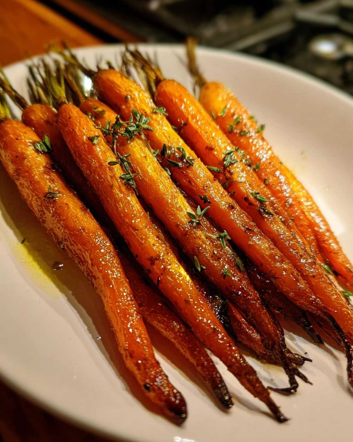 A close-up of glossy, glazed Balsamic Roasted Carrots served on a white plate, garnished with fresh thyme.