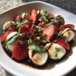 Close-up of fresh Balsamic Strawberry Caprese Salad featuring sliced strawberries, mozzarella balls, and basil drizzled with balsamic glaze.