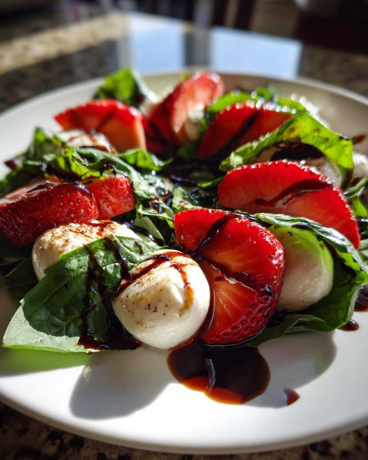 A vibrant close-up of Balsamic Strawberry Caprese Salad featuring fresh strawberries, mozzarella balls, and basil drizzled with balsamic glaze.