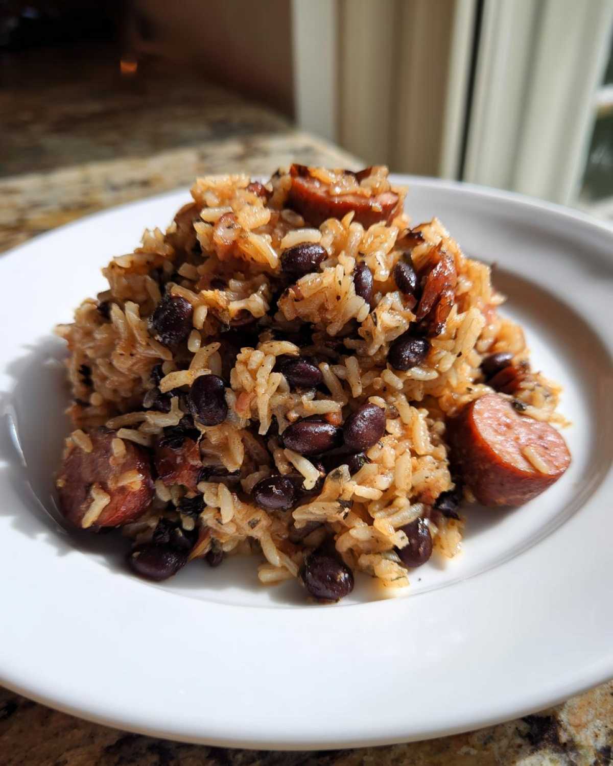 A close-up of a serving of seasoned beans and rice mixed with black beans and slices of smoked sausage.