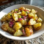 Close-up of the Best Roasted Potato Salad featuring golden roasted potatoes, red onion chunks, and herbs in a white bowl.