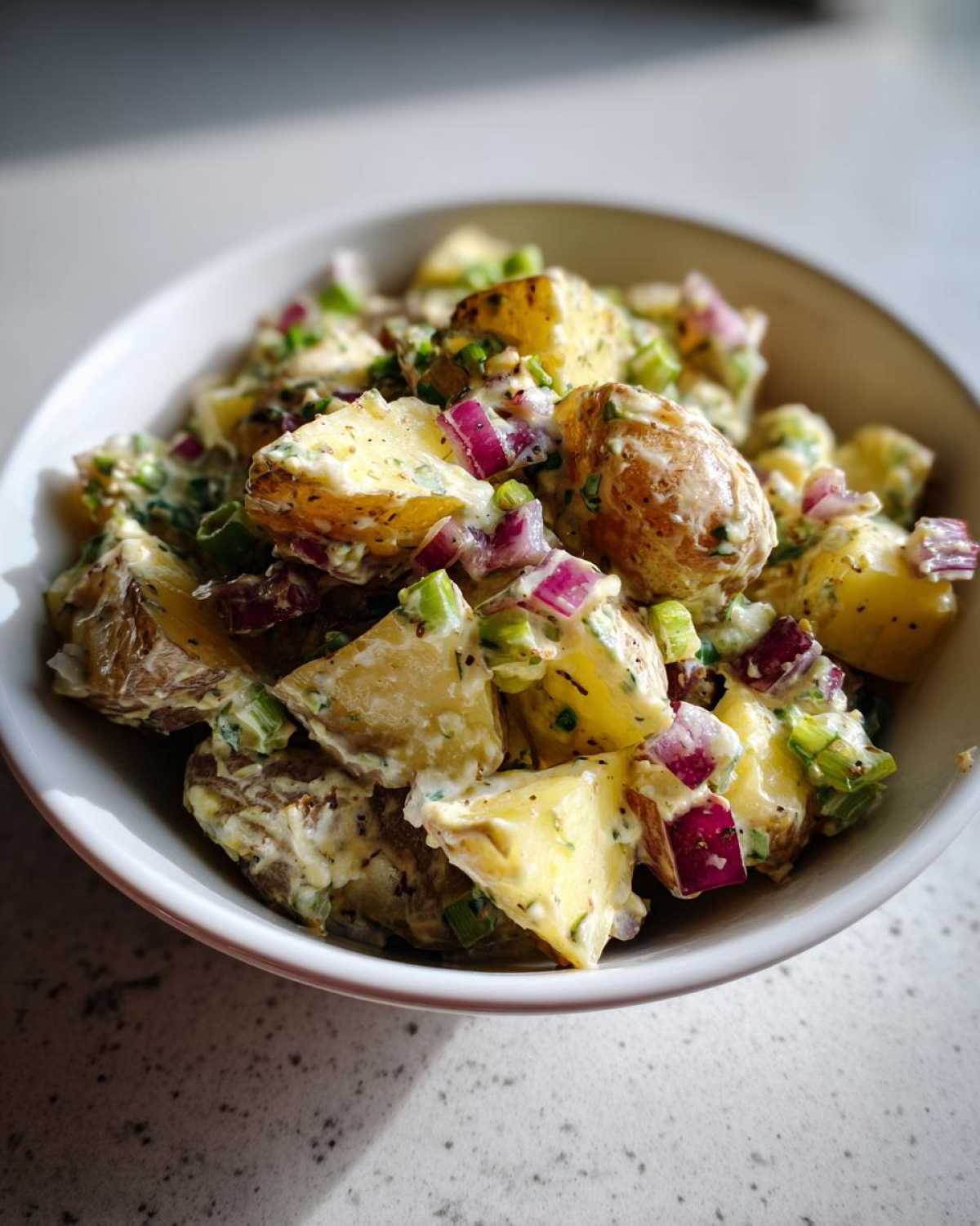 A close-up of the Best Roasted Potato Salad featuring roasted potatoes, red onion, and green onions coated in a creamy dressing.