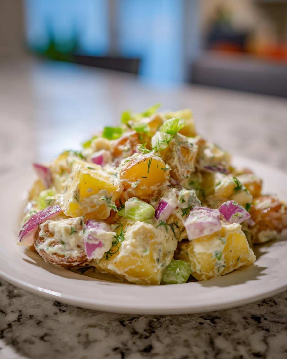 A serving of the Best Roasted Potato Salad featuring roasted potatoes, red onion, celery, and a creamy dressing, garnished with dill.