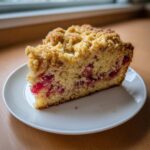 A close-up of a single slice of Big Crumb Rhubarb Coffee Cake, showing the thick crumb topping and pink rhubarb filling.