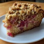 A close-up shot of a generous slice of Big Crumb Rhubarb Coffee Cake on a white plate.