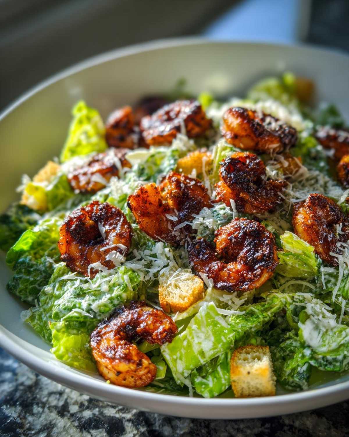 A close-up of a fresh Blackened Shrimp Caesar Salad topped with grated Parmesan cheese and croutons.